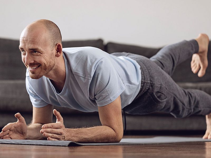 Mann macht eine Fitnessübung im Wohnzimmer und ist fröhlich